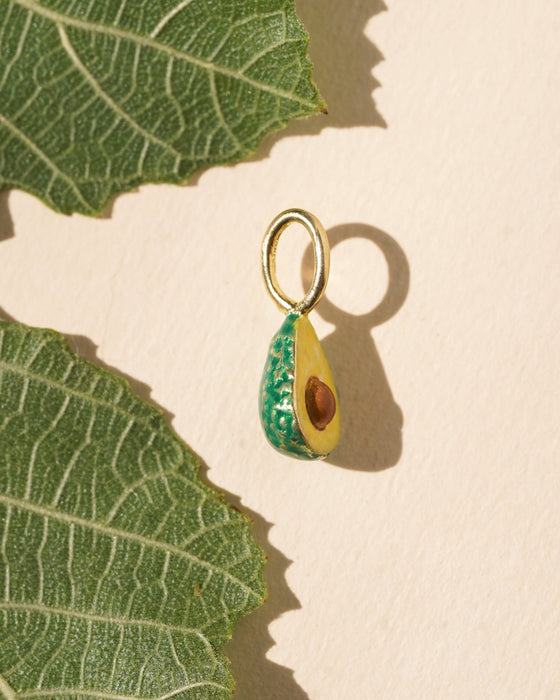 Avocado-shaped pendant with a gold chain on a beige background with a large green leaf.